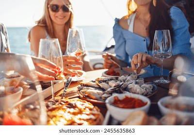 Festive banquet on board the ship. Close up of table with delicious food. Young smiling women raise toast with glasses of wine or cocktails. Fun bachelorette party on boat. Lunch during sea cruise. - Powered by Shutterstock