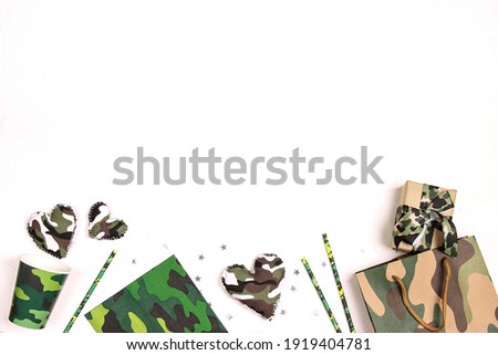 Festive border for Defender of the Fatherland Day, February 23. Party set with camouflage glasses, straws, napkins and gifts on white background with copy space for text.
