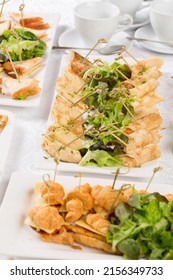 Festive Buffet. An assortment of cold snacks on wooden skewers. Decorated with lettuce leaves and served on rectangular plates against the background of saucer cups
