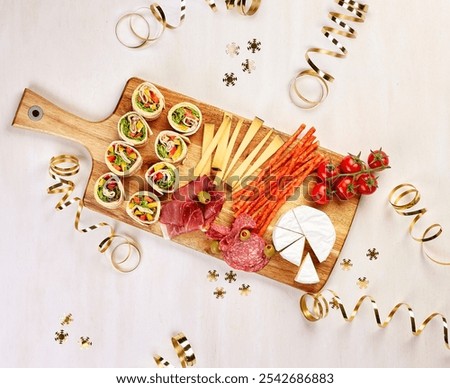 Festive charcuterie board featuring an array of snacks, including vegetable wraps, cheeses, salami, pepperoni sticks, cherry tomatoes, and olives, adorned with golden ribbons, perfect for celebration