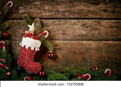 Festive Christmas Border With Colorful Patterned Red Boot Or Stocking Filled With Decorations, And A Gift On Rustic Wood Background With Pine And Candy Cane Border