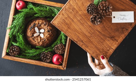 Festive Christmas cake in a wooden box, surrounded by pinecones and apples. Christmas cake, wooden box, pinecones, and apples create a holiday feel. Woman unboxing Christmas pudding gift. - Powered by Shutterstock