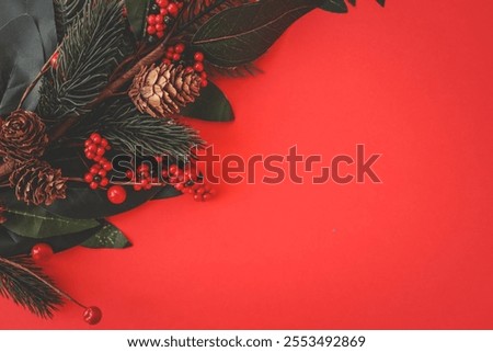 Festive Christmas composition featuring pinecones, red berries, and evergreen branches arranged on a vibrant red background, symbolizing holiday spirit and traditional decor.