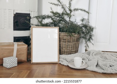 Festive Christmas Indoor Decor. Vertical Wooden Picture Frame Mockup On Parquette Floor. Pine, Larch Tree Branches In Basket, Gift Boxes. Cup Of Coffee. Old White Tiled Stove Background.Empty Template