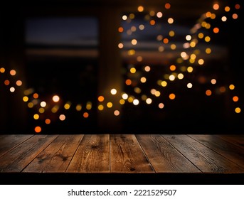 Festive, Christmas, New Year background. Evening. Night. 
 Homely, cozy background. Abstract background. A wooden table on the background of a window with a night view and golden garlands. Bokeh.  - Powered by Shutterstock