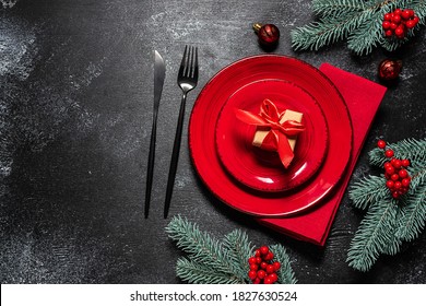 Festive Christmas or New Year table setting with cutlery set, red plates, gift box with bright bow and festive decorations on black rustic background top view. - Powered by Shutterstock