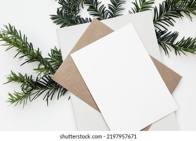 Festive Closeup Of Christmas Blank Greeting Card, Invitation Mockup Template. Craft Envelope, Diary And Green Yew Tree Branch Isolated On White Table Background. Winter Stationery. Flat Lay, Top View.