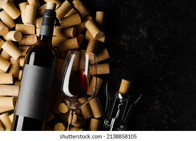 Festive composition. A bottle of red wine, a corkscrew and a wine glass lie on wine corks on a black background. There is free space to insert. Holiday, celebration, date, romantic evening. Banner.