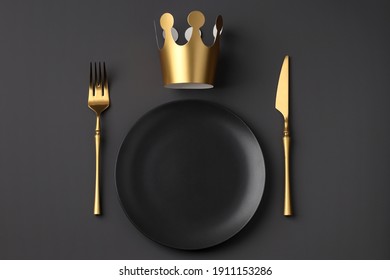 Festive creative royal table setting on a dark background. Gold crown, fork and knife. Valentine's Day, Wedding Day, Birthday, Women's Day and Mother's Day. Flat lay