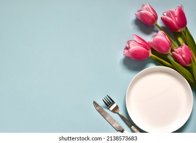 Festive creative table setting. Round plate and cutlery with tulip bouquet on blue background. Valentine's Day, Wedding Day, Birthday, Women's Day and Mother's Day. Flat lay. Copy space. Menu.