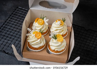 Festive cupcakes with cream cheese cream and citrus filling. Confectionery for the holiday. Dessert decorated with kumquat, rosemary and mastic snowflakes, packed in a gift box.