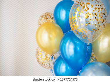 Festive decoration of a bright room with blue and transparent balloons with golden confetti. We celebrate the holidays at home. Bouquet of balloons on the background of wallpaper with zigzags