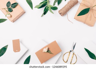 Festive Decorative Flat Lay Frame Of Gift Boxes, Green Leaves, Gold Scissors And Rose Flowers On White Background With Blank Center, Top View.