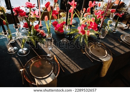 Festive dinner table is served dishes and cutlery and decorated with flowers tulips and greenery, candles. Birthday celebration. Family holidays in modern dining room. Stylish spring party. Wedding.