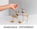 Festive DIY reindeer puppets made from cardboard tubes and bottle caps held by hand with wooden stick. Minimalist Christmas craft 