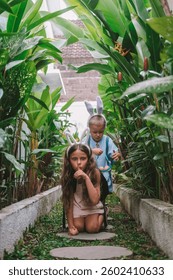 Festive Easter childrens game Egg hunt. Little brother and his older sister run along the path surrounded by tropical greenery in search of eggs, collect them in basket and have fun. Family traditions