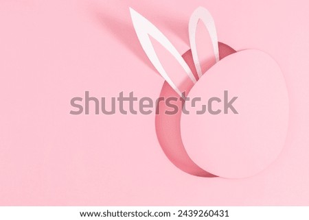 Festive Easter idea. Funny bunny ears protruding from an egg shaped oval hole on pastel pink background. Happy Easter.Top view. Flat lay.