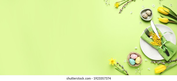 Festive Easter table setting with eggs and floral decor on green background, flat lay. Space for text
