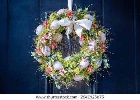 Festive Easter Wreath on Dark Door in Center. A vibrant Easter wreath adorned with speckled eggs, pink flowers, and butterflies hangs on a dark door, celebrating spring and holiday decor.