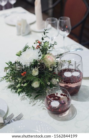 festive flower composition with eustoma, rose, pistachio, thuja, waxflower, holly, pinecones, chrysanthemum, Eucalyptus parvifolia,float candle, on table for winter dinner indoors, stock photo image