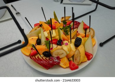 Festive Fruits Plate With Cut Fruit Pieces On Skewers In White Plate. Dessert For Birthday Party, Sweet Appetizer. Banana, Apple, Pear And Prunes, Orange, Strawberry And Mint