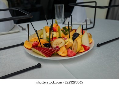 Festive Fruits Plate With Cut Fruit Pieces On Skewers In White Plate. Dessert For Birthday Party, Sweet Appetizer. Banana, Apple, Pear And Prunes, Orange, Strawberry And Mint