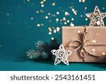 Festive gift box with pine branch and stars on teal background with bokeh lights