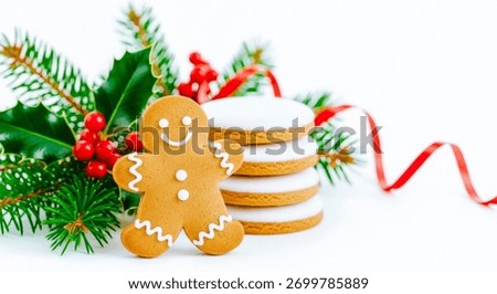 A festive gingerbread man and a stack of iced cookies are arranged with holly and ribbon, capturing the essence of the holiday season in a sweet and decorative scene.