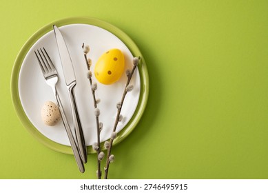 Festive Happy Easter table setting with painted eggs, pussywillow branches and stainless cutlery arranged on green backdrop for spring celebration