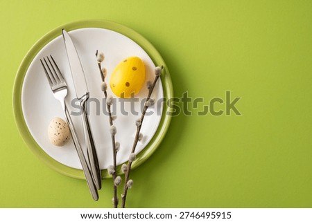 Festive Happy Easter table setting with painted eggs, pussywillow branches and stainless cutlery arranged on green backdrop for spring celebration
