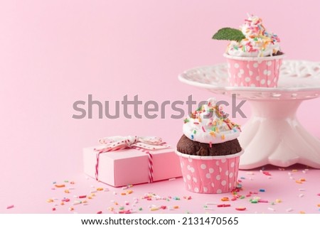 Festive holiday cupcakes for Birthday, Woman or Mothers Day. Pink paper decorations, sweet chocolate cupcakes with sprinkles and gift boxes on pink background. Party time concept.