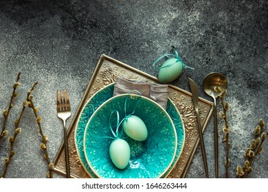 Festive holiday table setting for Easter dinner decorated with colored eggs on stone background with copy space