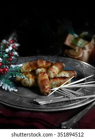 Festive image of commonly termed Pigs in Blankets. Cocktail pork sausages wrapped in bacon and grilled. Wooden cocktail sticks to spike them and eat. Against a rustic background with copy space.