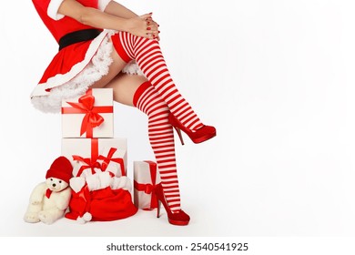 Festive image of a woman in a Santa costume with red striped stockings and high heels. Presents and a teddy bear enhance the Christmas theme. Isolated on white background with copy space. - Powered by Shutterstock