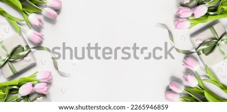 festive layout with tulips and a gift with green ribbons on a grey background. copy space. top view. flat lay. concept of mother's day, valentines day, eighth of march