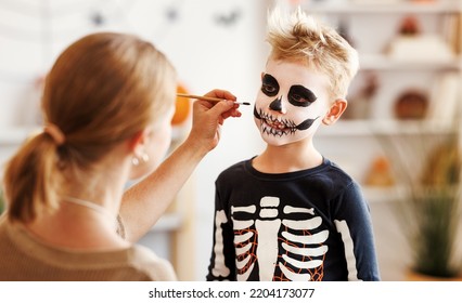 Festive makeup for Halloween. Woman doing skeleton make-up    for a little cheerful boy in costume while preparing holiday at home. - Powered by Shutterstock