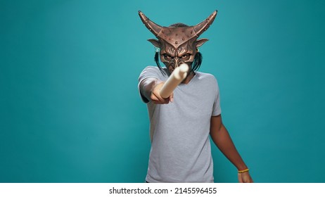 Festive Man With Traditional Ceremonial Mask Using Paddle, Standing Over Blue Background. Cheerful Person Wearing Indigenous Artifact Used In Tribal History To Create Ancient Native Ritual.