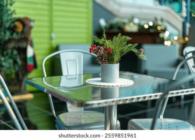 A festive natural Christmas centerpiece on a white doily with greenery, red berries, fir, pine cones and buds. The arrangement is on a square silver metal restaurant table with four metal chairs.  - Powered by Shutterstock