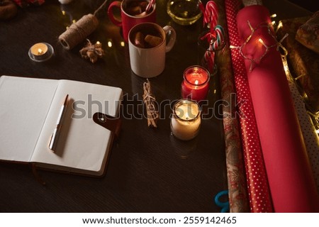 Festive notebook and holiday-themed items such as wrapping paper, candles, and cups on a table.