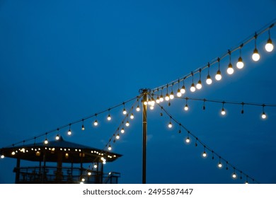 Festive outdoor lighting decor with string of glowing bulbs or lanterns for a cozy night holiday event. Warm,atmospheric,and romantic ambiance. - Powered by Shutterstock