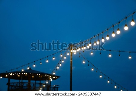 Festive outdoor lighting decor with string of glowing bulbs or lanterns for a cozy night holiday event. Warm,atmospheric,and romantic ambiance.