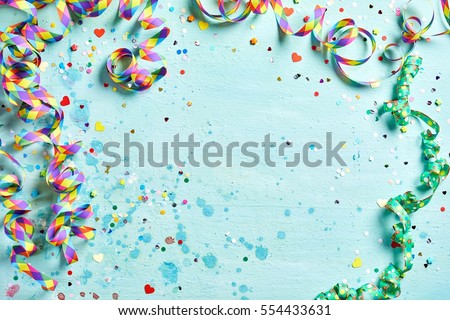 Festive party or carnival border of coiled streamers and confetti on a light blue green wood background with copy space