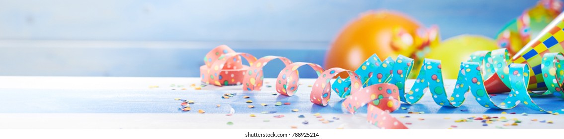 Festive party celebration banner with colorful balloons, streamers and scattered confetti on a white wood surface with copy space in a wide angle panorama