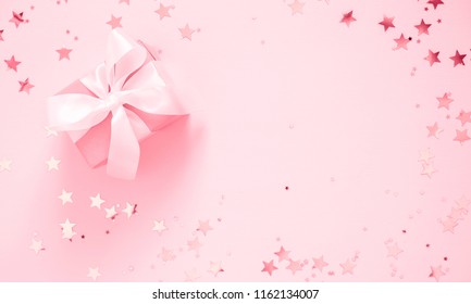 Festive pink background. Gift with satin bow and shining stars on light pink pastel background. Christmas. Wedding. Birthday. Happy woman's day. Mothers Day. Valentine's Day. Flat lay, top view