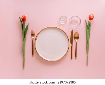 Festive pink table setting. Pink plate with gold cutlery and red tulip on pink background. Aesthetic stylish dinner table setting for Women's day, Mother's Day,wedding or anniversary.Copyspace topview - Powered by Shutterstock