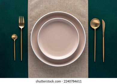 Festive place setting with beige napkin. Empty plates and gold cutlery on dark green background. Top view. Dining table in luxury restaurant. Card or menu template, flat design. Tableware, crockery. - Shutterstock ID 2240784611