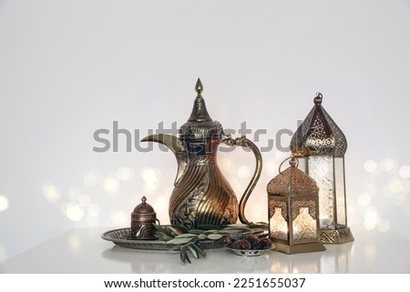 Festive Ramadan Kareem, Iftar dinner still life. Glowing Moroccan ornamental lanterns, arabic dallah coffee pot. Olive tree branches, date fruit on silver tray. Blurred background, golden bokeh lights