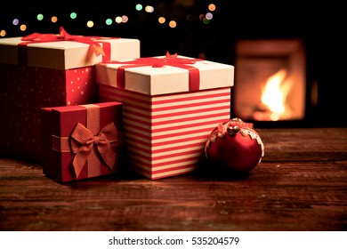 festive red Gift Boxes standing by the Burning Fireplace and Christmas tree - cozy home
