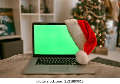 A festive scene with a laptop with green screen wearing a Santa hat, surrounded by Christmas decorations, ideal for holiday marketing to spread joy and warmth during the enchanting festive season - Powered by Shutterstock