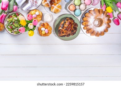 Festive served Easter dinner or brunch table, with Easter egg, tulip flower bouquet, traditional Easter foods - cake, cross buns, wreath bread, glazed ham and spring salad, white table background - Powered by Shutterstock